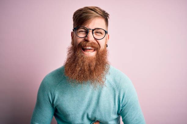 handsome irish redhead mann mit bart trägt brille über rosa isolierten hintergrund lächelnd und lachen hart laut, weil lustig verrückt witz mit händen auf körper. - european culture audio stock-fotos und bilder