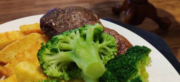 ECU of broccoli sitting on top of a sirloin steak with chips, on a plate