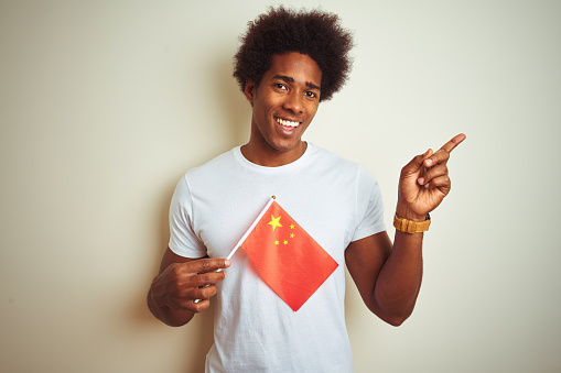 Young afro american man holding China Chinese flag standing over isolated white background very happy pointing with hand and finger to the side