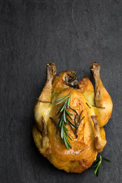 Roasted  poussin with rosemary on black stone background