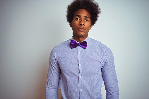 Afro business man wearing striped shirt and purple bow tie over isolated white background with serious expression on face. Simple and natural looking at the camera.