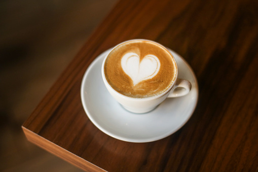 Espresso coffee with heart shaped froth art on a wooden table in a cafe.