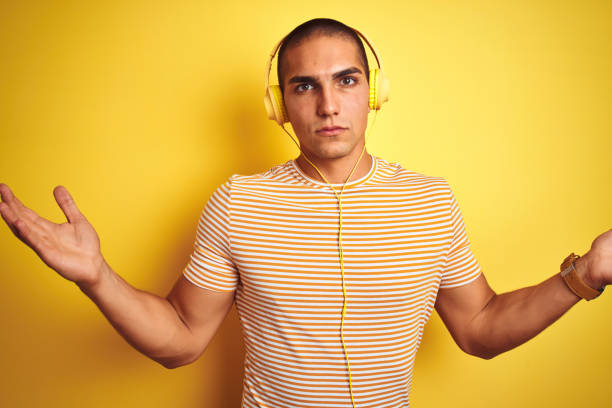 istock Young handsome man using headphones over yellow isolated background clueless and confused expression with arms and hands raised. Doubt concept. 1205026275