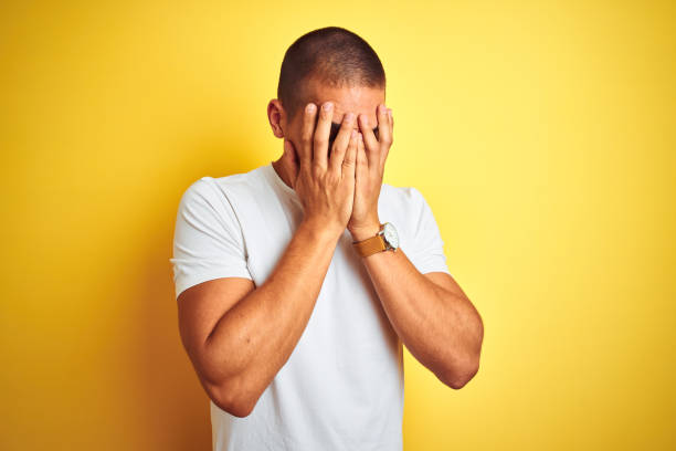 joven caucásico con camiseta blanca casual sobre fondo aislado amarillo con expresión triste cubriendo la cara con las manos mientras llora. concepto de depresión. - avergonzamiento fotografías e imágenes de stock