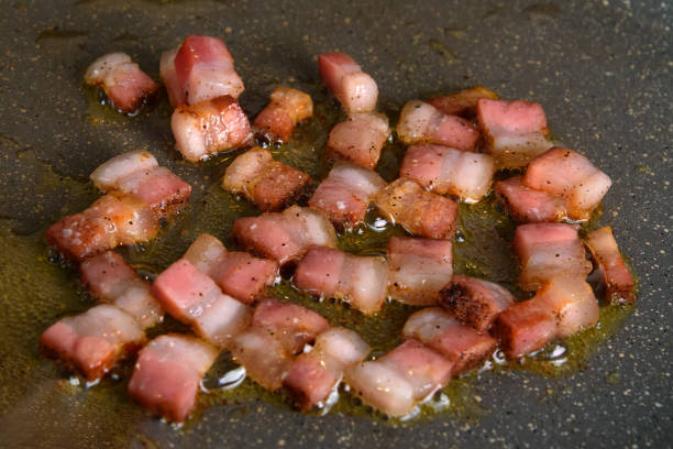 istock Selective focus. Fried crispy bacon/pancetta, sliced ​​in small squares, fried in a gray pan. Close up 1205026618