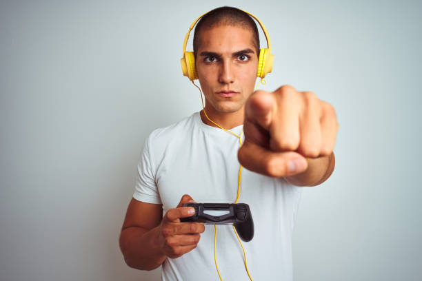 istock Young handsome man playing videogames using headphones over white isolated background pointing with finger to the camera and to you, hand sign, positive and confident gesture from the front 1205026762
