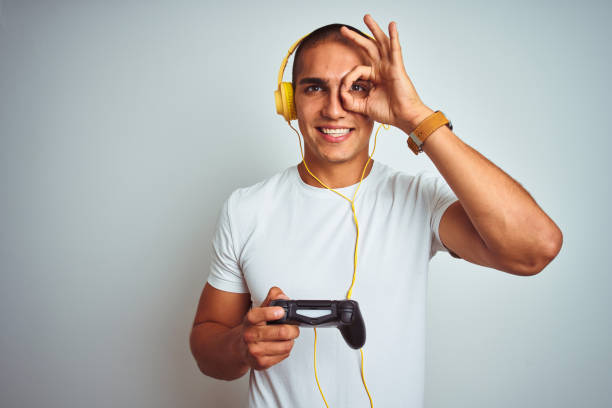 istock Young handsome man playing videogames using headphones over white isolated background with happy face smiling doing ok sign with hand on eye looking through fingers 1205026804