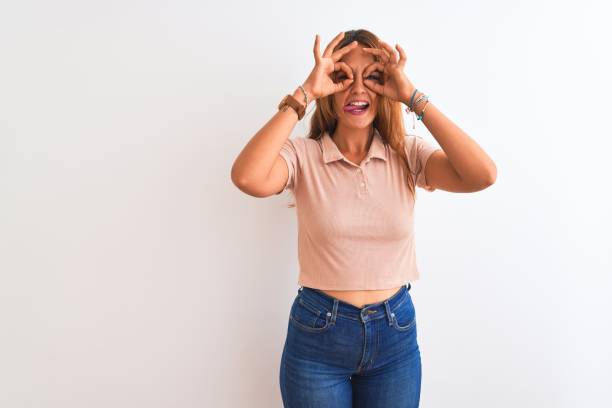 istock Young redhead woman stading over white isolated background doing ok gesture like binoculars sticking tongue out, eyes looking through fingers. Crazy expression. 1205028893