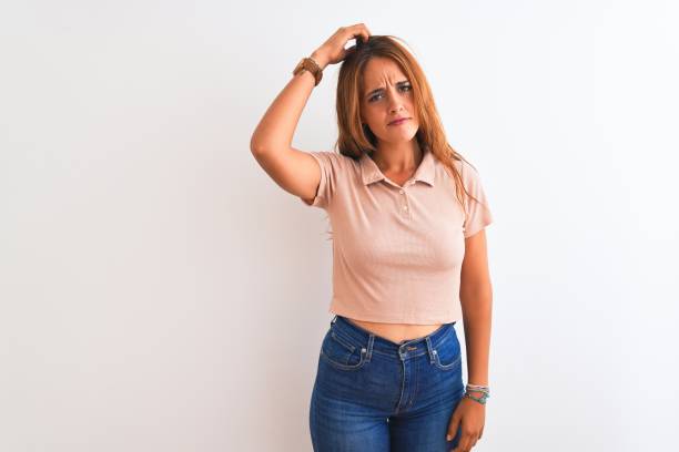 Young redhead woman stading over white isolated background confuse and wonder about question. Uncertain with doubt, thinking with hand on head. Pensive concept.
