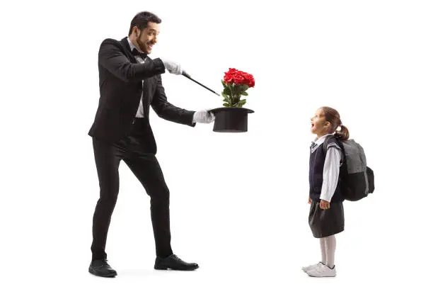 Full length shot of a magician making a magic trick with roses and an excited schoolgirl watching isolated on white background