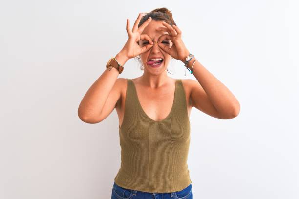 istock Young redhead woman wearing a bun over isolated background doing ok gesture like binoculars sticking tongue out, eyes looking through fingers. Crazy expression. 1205028991