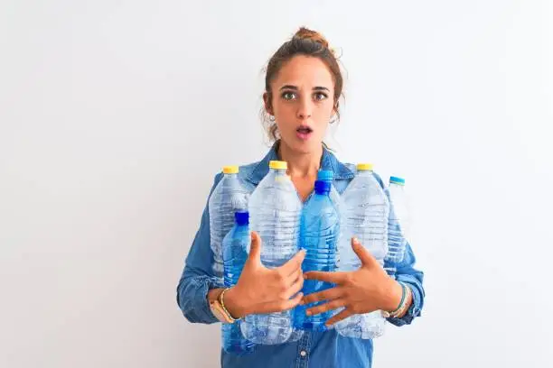 Photo of Young redhead woman holding plastic bottle to recycle over isolated background scared in shock with a surprise face, afraid and excited with fear expression