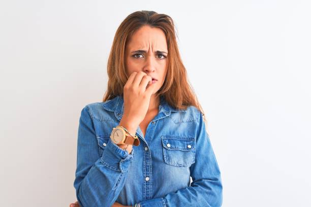 istock Young redhead woman wearing denim jacket standing over isolated background looking stressed and nervous with hands on mouth biting nails. Anxiety problem. 1205031375
