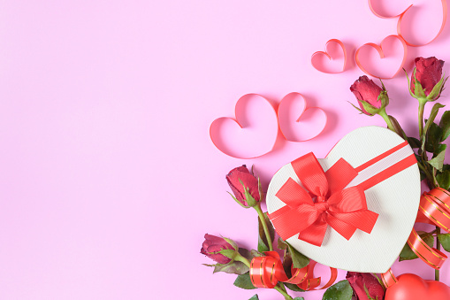 Red roses and gift box with heart red ribbon on pink background, copy space and Valentine's day background concept