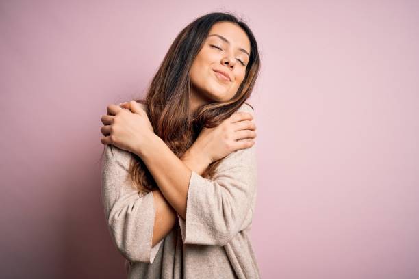 young beautiful brunette woman wearing casual sweater standing over pink background hugging oneself happy and positive, smiling confident. self love and self care - self love imagens e fotografias de stock