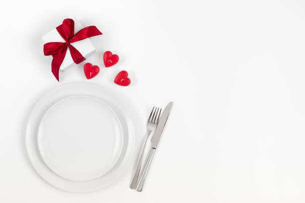 istock Valentines day or romantic dinner background. Festive romantic table setting with candles in the shape of hearts and a gift on a white background. 1205033119