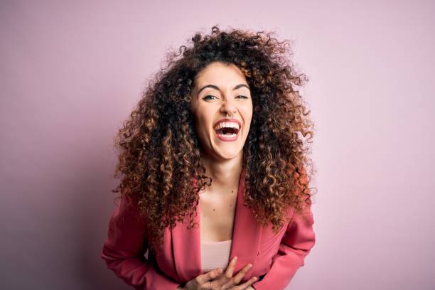 Young beautiful businesswoman with curly hair and piercing wearing elegant jacket smiling and laughing hard out loud because funny crazy joke with hands on body. Young beautiful businesswoman with curly hair and piercing wearing elegant jacket smiling and laughing hard out loud because funny crazy joke with hands on body. people laughing hard stock pictures, royalty-free photos & images