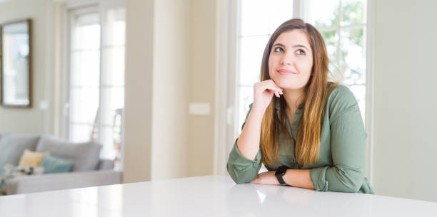 istock Beautiful young woman at home with hand on chin thinking about question, pensive expression. Smiling with thoughtful face. Doubt concept. 1205038435