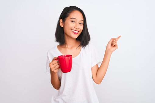 Young beautiful chinese woman drinking cup of coffee over isolated white background very happy pointing with hand and finger to the side