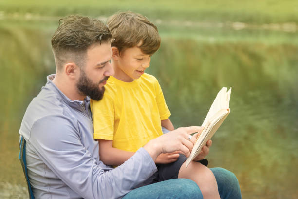 istock young man reading a book with a boy in nature 1205039177