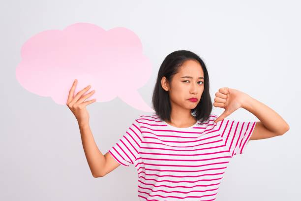istock Young chinese woman holding cloud speech bubble standing over isolated white background with angry face, negative sign showing dislike with thumbs down, rejection concept 1205039183