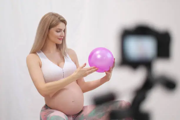 Photo of A sporty pregnant young woman blogger talks about ball exercises.