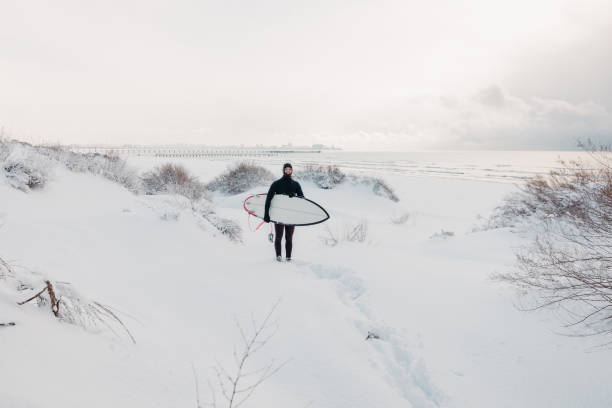 istock Cold winter and surfer with surfboard. Snowy day with surfer in wetsuit. 1205045708