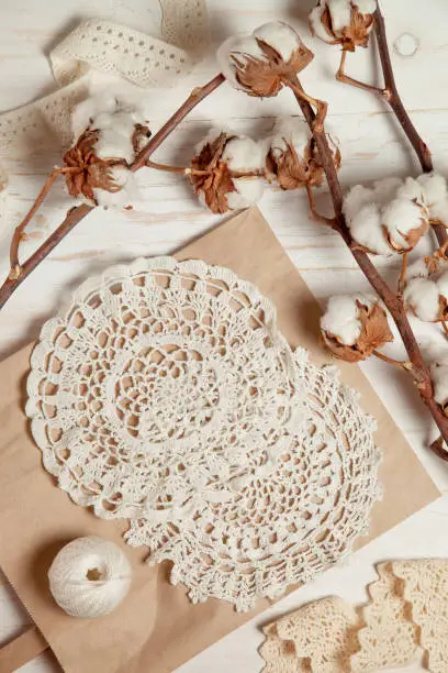 Hobby concept. handmade crocheted white napkins and cotton branches on a wooden background. top view.