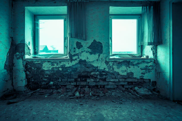 Viewing in an old room with big windows. Empty place in an abandoned building. Bricks come through the wall plaster and paint is peeling off. Ruined apartment in bad condition.