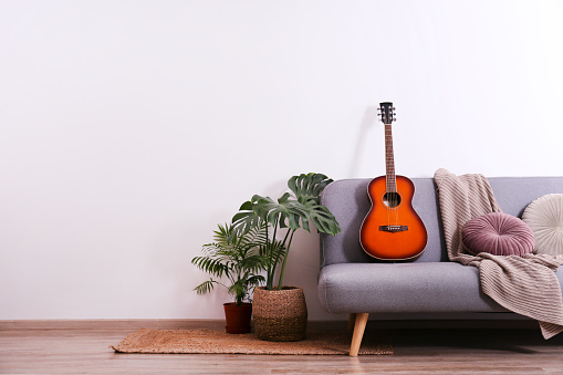 Minimalistic interior design concept. Acoustic guitar on grey textile sofa in spacious room of loft style apartment with wood textured laminated flooring. Background, copy space, close up.