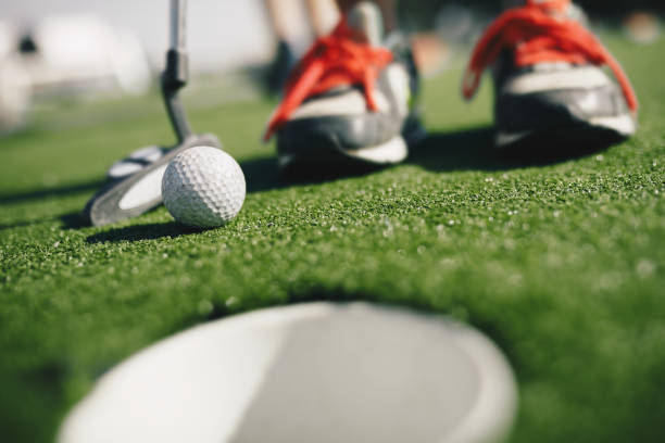 kinder spielen minigolf. nahaufnahme des spielers in snickers mit minigolfschläger und weißem golfball. e tasse im vordergrundgoldloch th - putting golf golfer golf swing stock-fotos und bilder