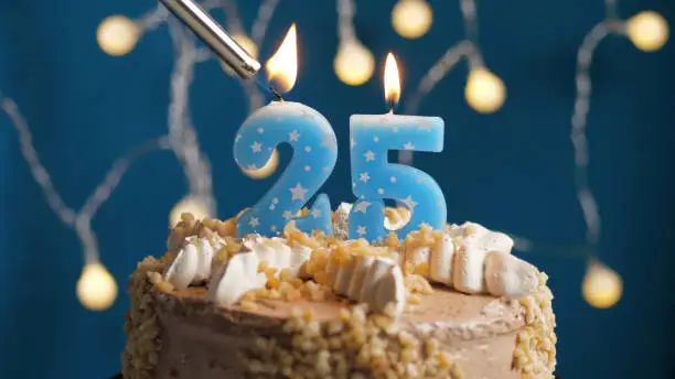 Photo of Birthday cake with 25 number candle on blue backgraund set on fire by lighter. Close-up