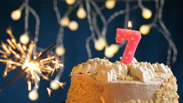 Photo of Birthday cake with 7 number pink candles and burning sparkler on blue backgraund. Close-up