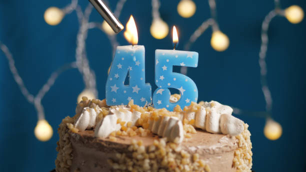 istock Birthday cake with 45 number candle on blue backgraund set on fire by lighter. Close-up 1205065747