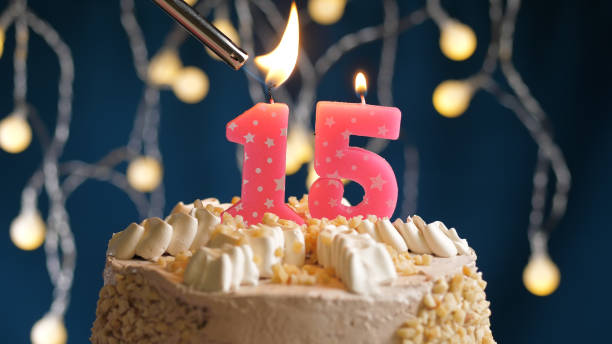 istock Birthday cake with 15 number pink candle on blue backgraund set on fire by lighter. Close-up view 1205065801