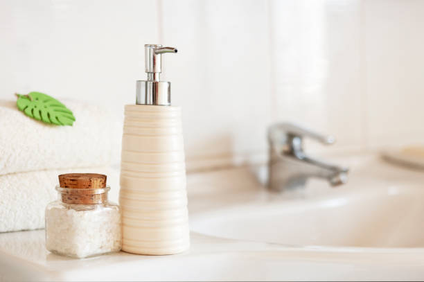 istock Ceramic soap, shampoo bottle, glass bottle with bath salt and white cotton towels on Blurred bathroom interior background with sink and faucet. 1205067241