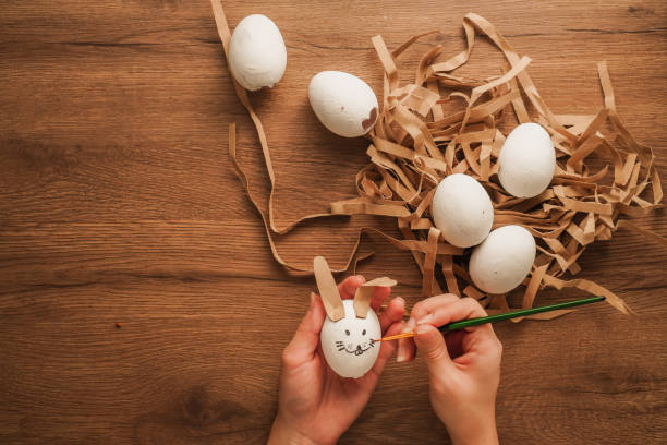 istock painting an egg in hand like a rabbit face and other white egg on wooden table 1205073878