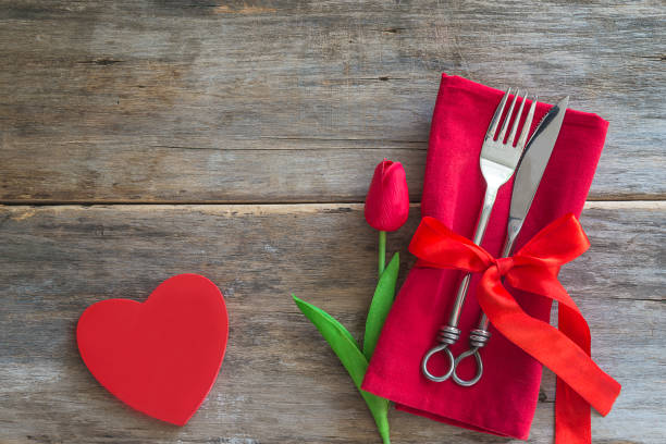 Festive table setting for valentine's day dinner. Festive table setting for valentine's day dinner. Fork and knife, red napkin, red tulip and heart on old wooden background. Copy space, top view book heart shape valentines day copy space stock pictures, royalty-free photos & images