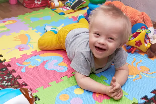 Photo of Closeup of happy smiling baby boy crawling on colorful playmat. child on a play mat with toys. smiling child with down syndrome.