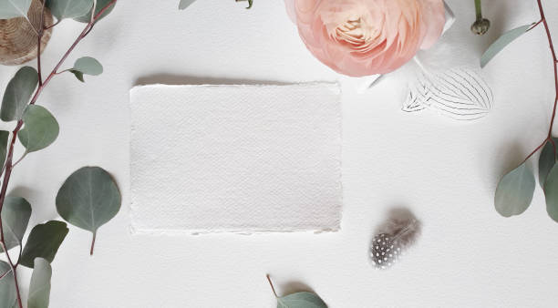 istock Blank white Wedding Greeting invitation card mockup silver eucalyptus leaves branch, blush pink buttercup ranunculus flower on textured paper table backgound. Elegant modern template Flat lay top view 1205076694