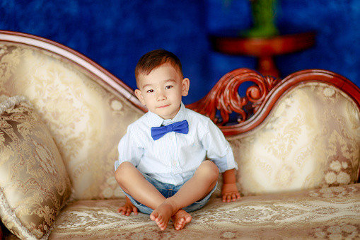 Boy is a child of Asian appearance. The boy 4-5 years Asian looks dressed as a gentleman and sits on the sofa.