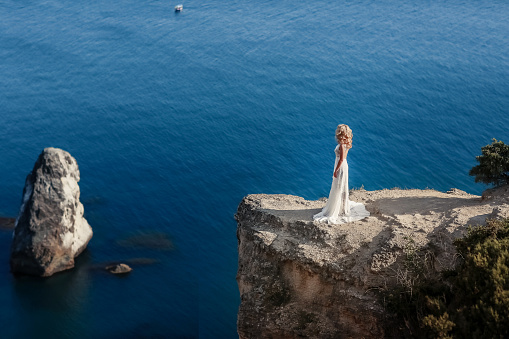 Woman in dress at the top of the mountain. Beautiful girl dressed in a white dress stands on top of the mountain above the ocean