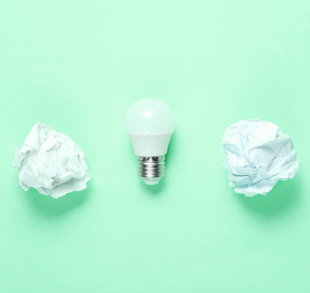 istock Energy saving LED light bulb and crumpled paper balls on green background. Minimalistic business concept, idea. Top view 1205081365