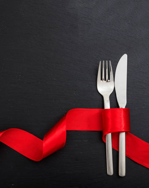 istock Valentine day dinner table setting. Fork and knife cutlery tied with red ribbon on black background, top view. 1205082845