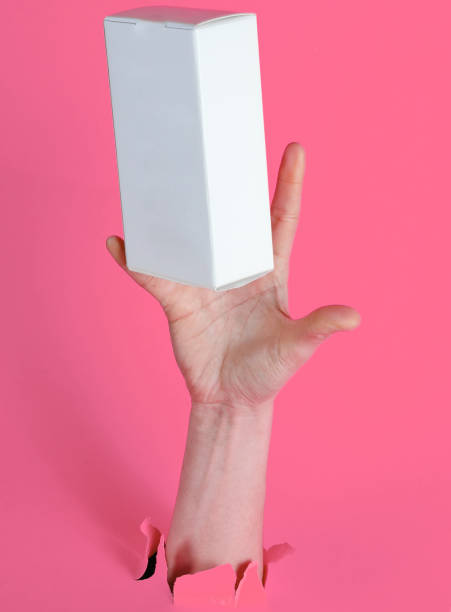 istock Female hand catches white box through torn pink paper. Minimalistic creative concept 1205084281