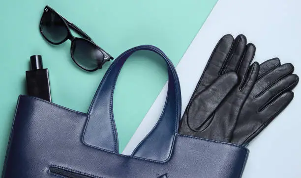 Photo of Leather bag, sunglasses, gloves, perfume bottle on gray- blue background. Women's fashion accessories