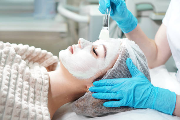 cosmetologist doing cosmetic face mask treatment for the young woman. - exfoliating scrub imagens e fotografias de stock