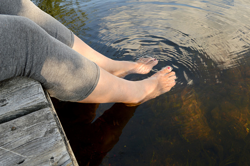 A woman splashes her feet in the cool river water as she rests on the dock during the heat of the summer.