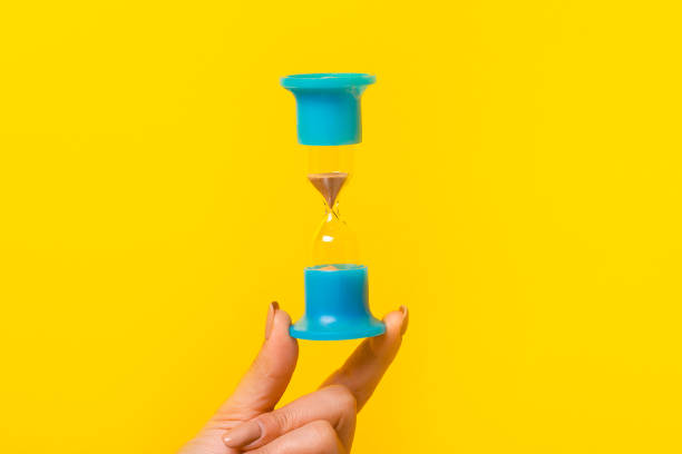 hourglass in hand over yellow background, transience of time concept