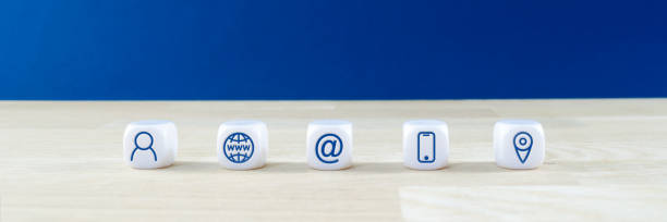 istock Wide view image of customer service image with five white dices with www, contact information and location icons on them. On solid oak table, over blue background. 1205100074